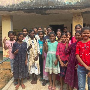 Un groupe de jeunes filles souriantes posant devant un bâtiment scolaire dans une ambiance chaleureuse et amicale, symbolisant l'accès à l'éducation et l'empowerment des jeunes filles.